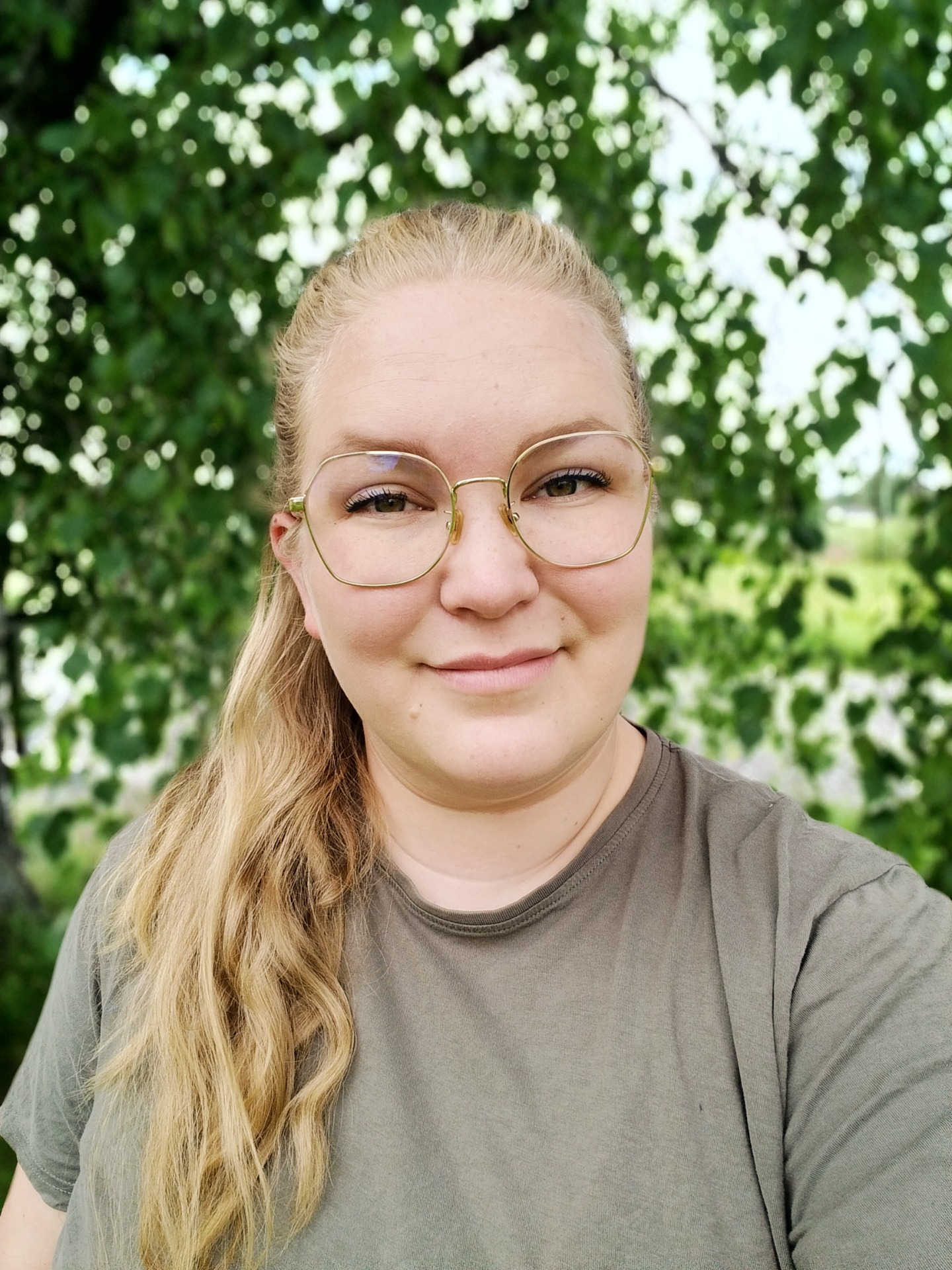 Blondi nainen pyöreissä kultakehyksisissä laseissa, lähikuva vihreässä puutarhataustassa, pehmeä bokeh.